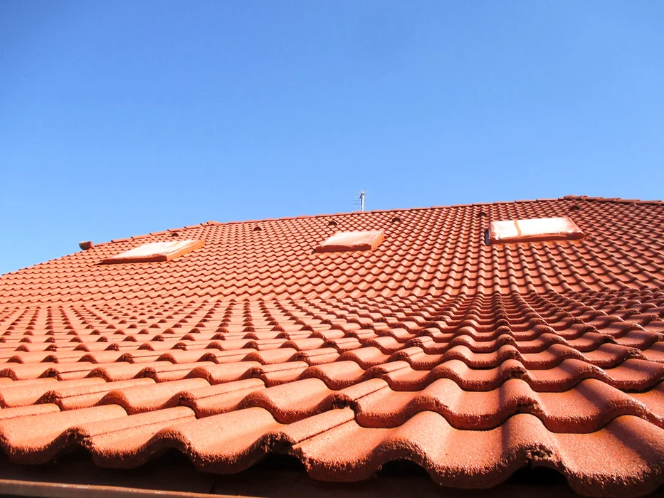 Toiture en tuiles canal terre cuite rouge-orangé, vue en contre-plongée sous ciel bleu dégagé