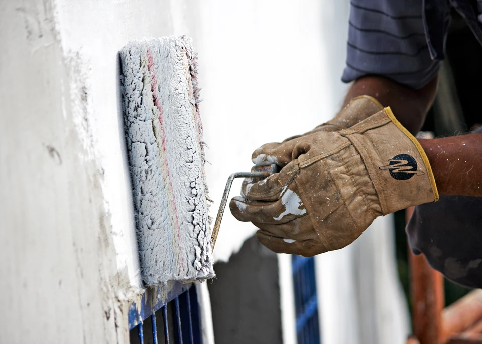 Chantier extérieur avec ouvrier appliquant un enduit ou mortier sur mur blanc à l'aide d'un rouleau de peinture