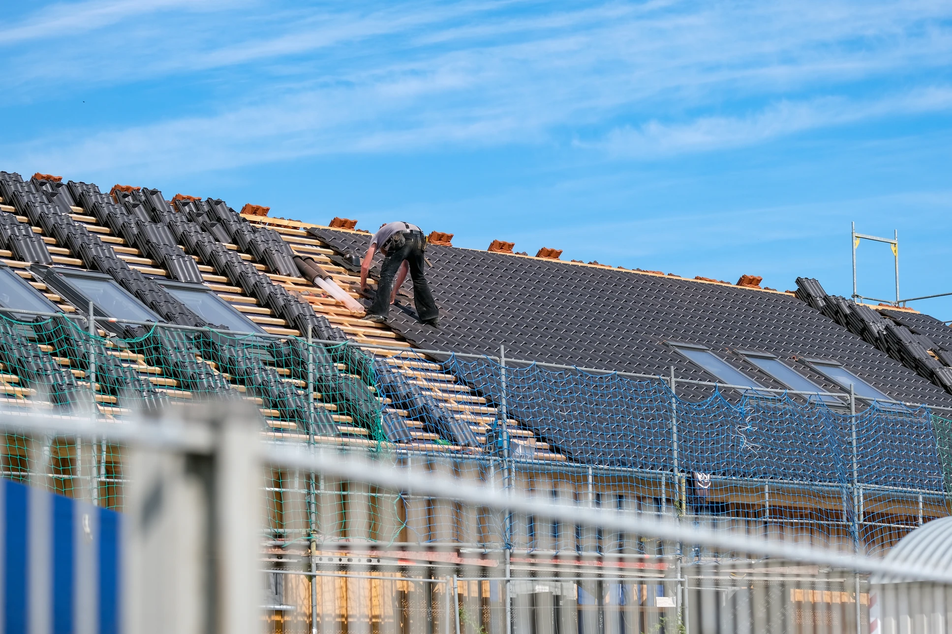 Chantier de construction résidentielle en extérieur avec ouvrier couvreur installant des tuiles grises sur charpente en bois