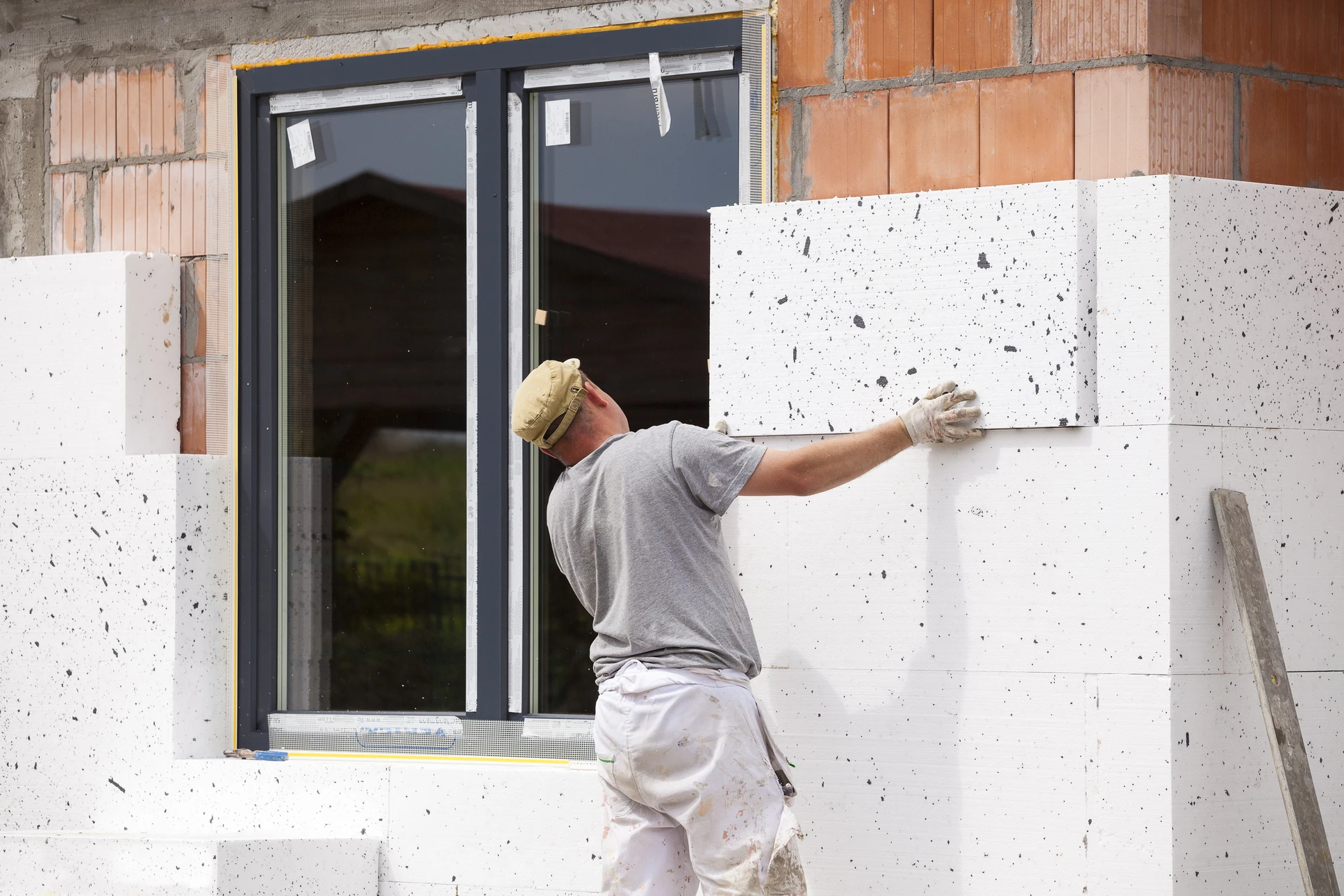 Homme en vêtements de travail effectuant des travaux de peinture extérieure sur façade blanche de maison moderne