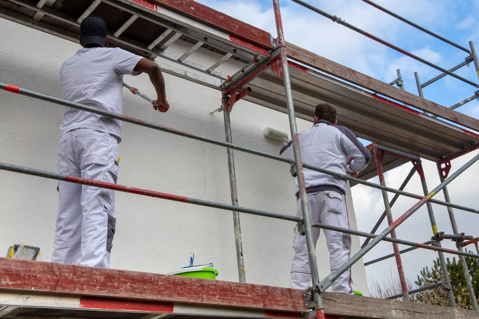 Deux peintres en bâtiment travaillent sur échafaudage tubulaire contre façade de maison