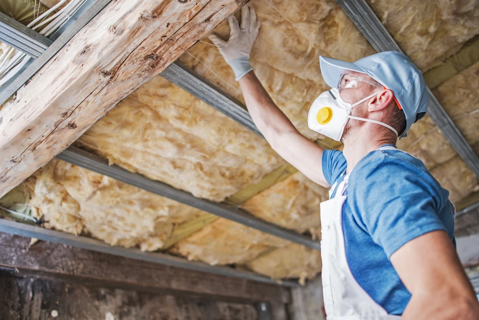 Ouvrier en équipement de protection individuelle installant de l'isolation thermique dans les combles d'une habitation