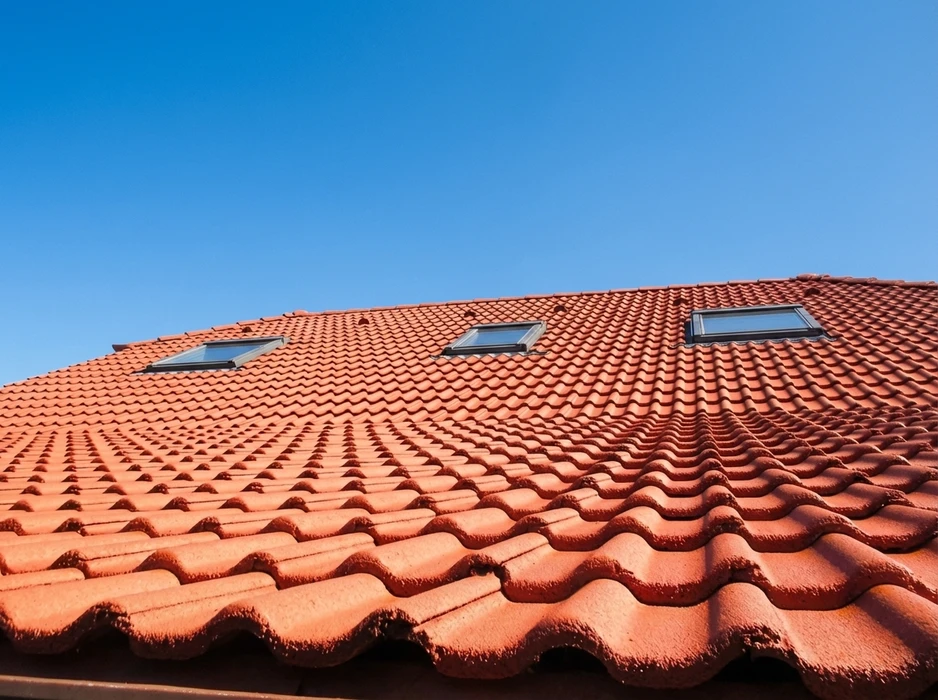 Toiture en tuiles canal terre cuite rouge-orangé, vue en contre-plongée, ciel bleu dégagé