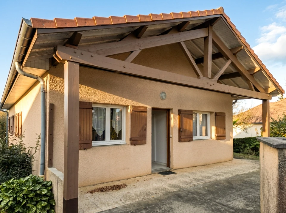 Façade pignon d'une maison individuelle, enduit monocouche ton sable, toiture à deux pans en tuiles canal terre cuite, chevrons apparents, chéneau zinc