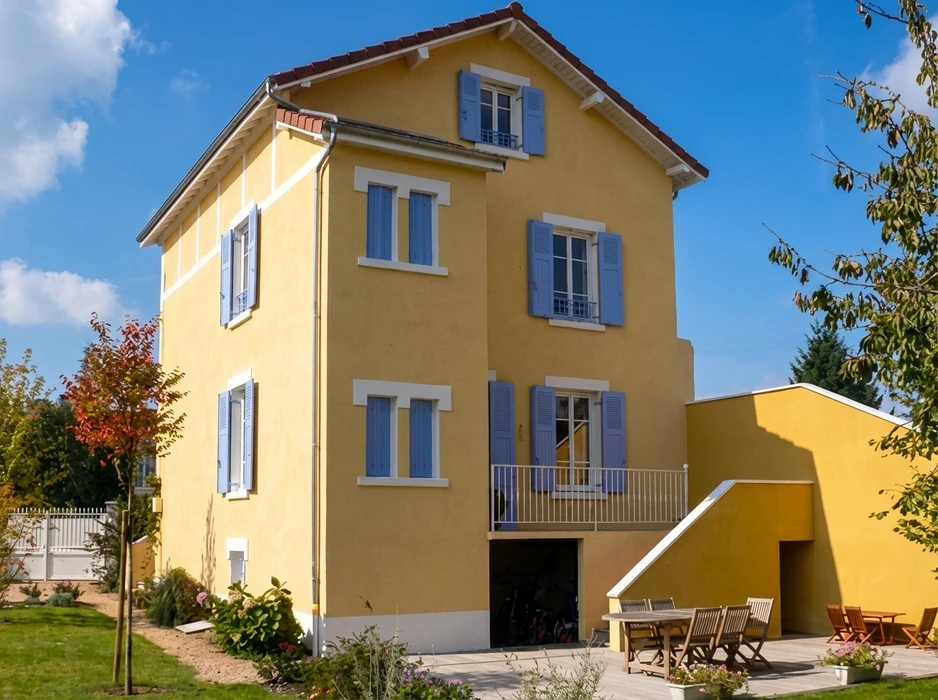 Façade extérieure d'une maison individuelle plain-pied, enduit monocouche beige, volet roulant PVC blanc sur fenêtre à appui, porte d'entrée avec auvent tuiles canal, rampe d'accès PMR acier blanc