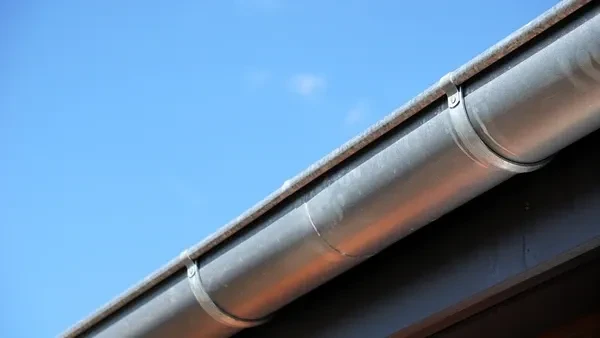 Ouvrier en bâtiment sur toiture installant une gouttière métallique grise